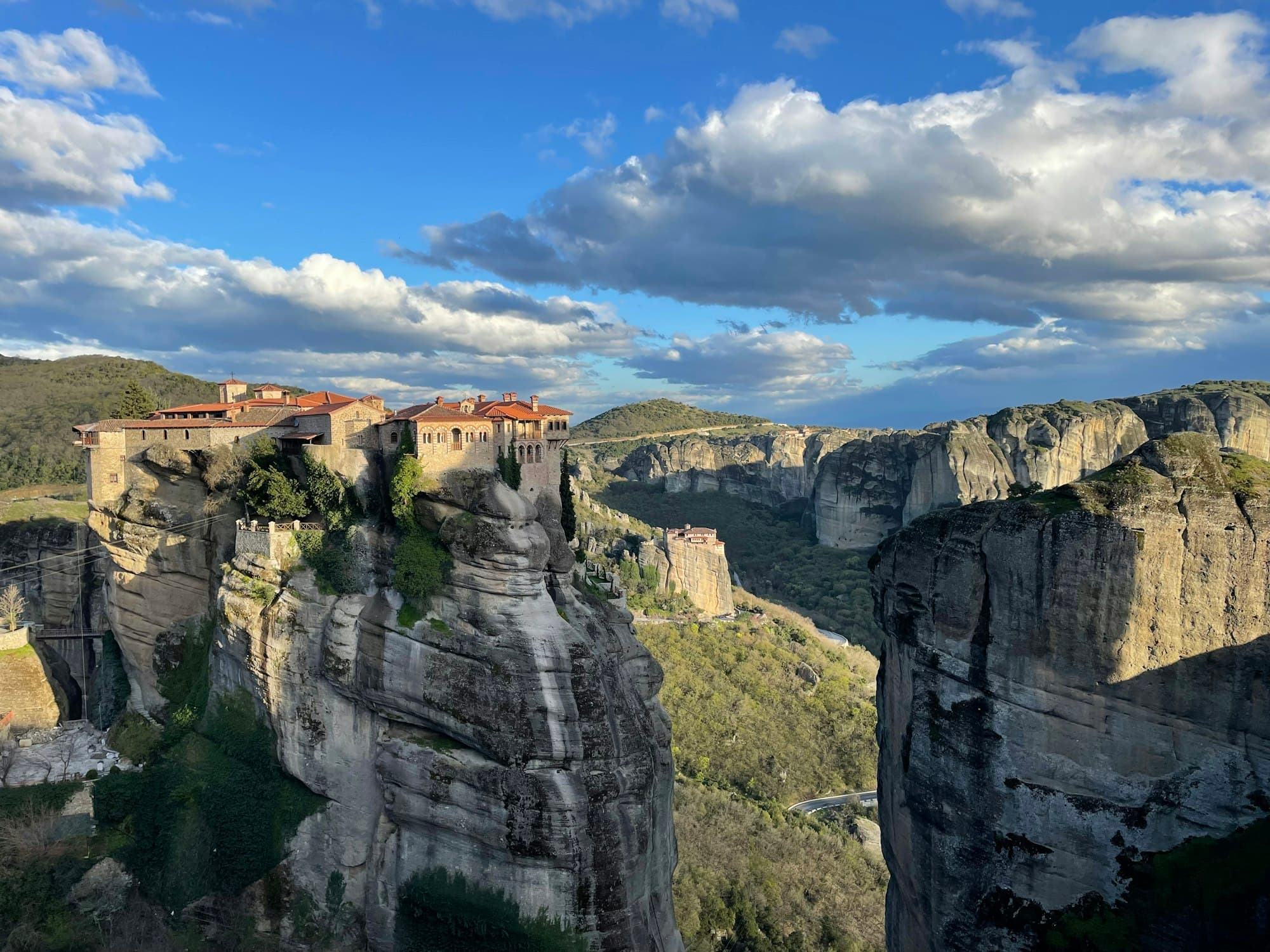 Monastery with red tile roofs on a sandstone pillar at Meteora, a second monastery and rock towers behind.
