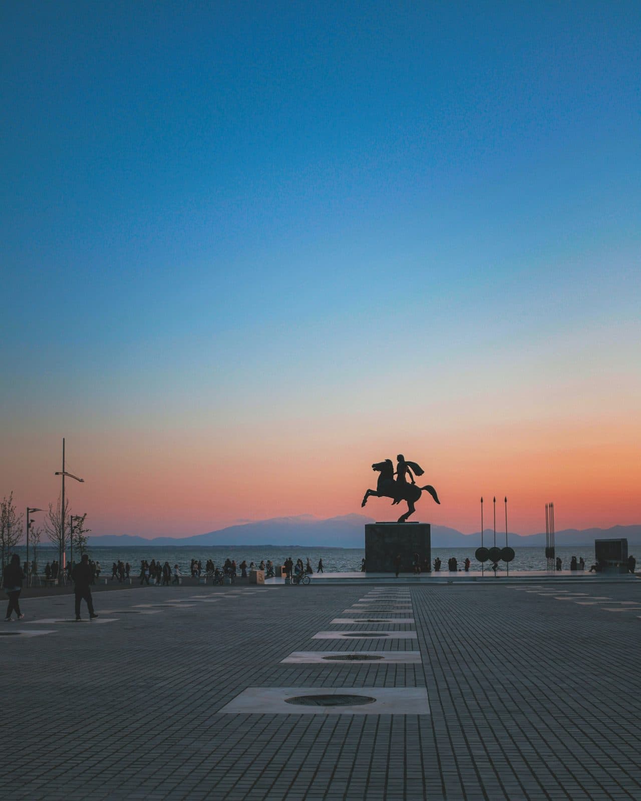 The equestrian statue of Alexander the Great on the Nea Paralia, with people walking at sunset